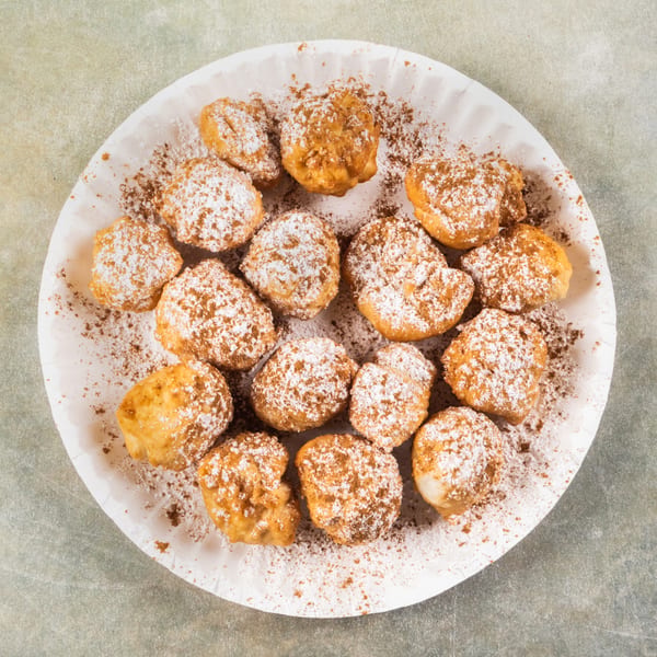 A white paper plate filled with golden-brown fried dough balls, dusted with powdered sugar and cinnamon.