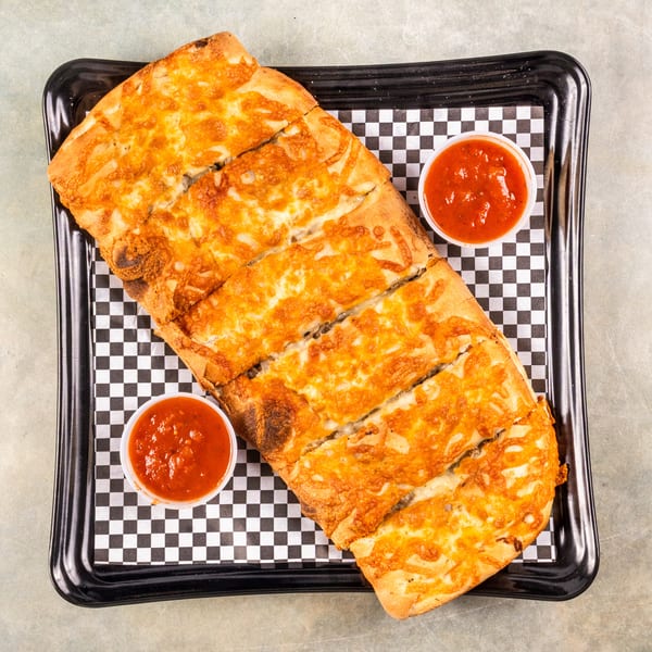 Cheesy breadsticks, cut into strips, served with two cups of marinara sauce on a checkered paper.