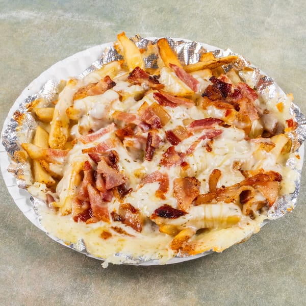 Loaded fries with melted cheese and crispy bacon bits in a foil-lined paper plate.