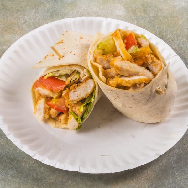 Two chicken wraps filled with crispy chicken, lettuce, and tomatoes on a white paper plate.