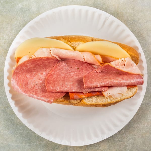 Overhead view of a deli sub sandwich with salami, ham, and cheese on a paper plate.
