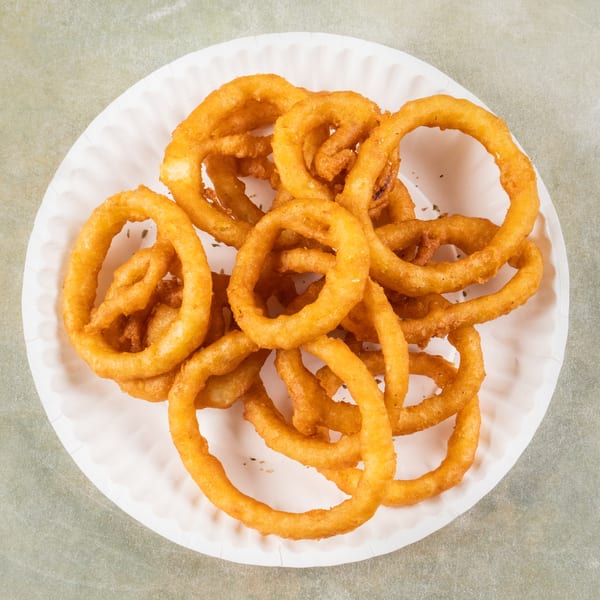 A white paper plate piled high with golden-brown, crispy onion rings, viewed from above.